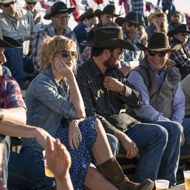beth rip and john dutton attend a rodeo they are sitting in the stands beth is wearing a blue and white print dress with suede boots a worn jeans jacket and sunglasses