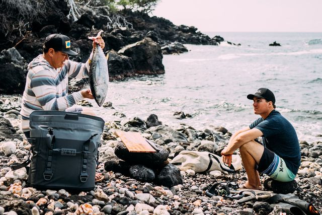man taking fish out of yeti hopper bag by beachside with a friend