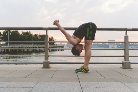 Young man practicing yoga bending down and arms raised at riverside