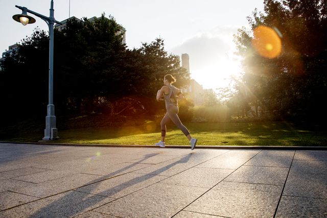 young active woman running in city park in morning light