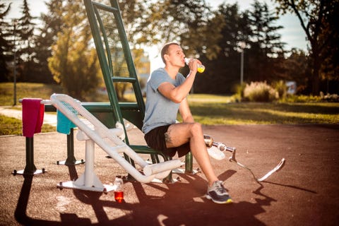 Young adaptive sportsman hydrating himself and resting during an exercise in a public park gym Young adaptive sportsman hydrating himself and resting during an exercise in a public park gym