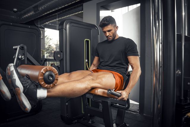 young adult man doing leg extension exercise in gym
