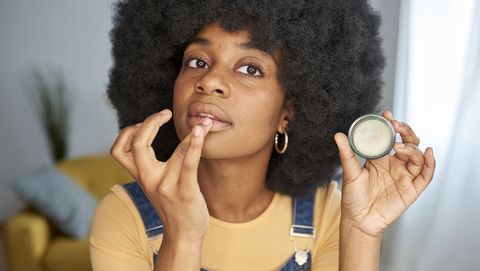 young afro woman applying lip balm on her lips while doing her make up at home
