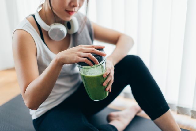 young asian woman drinking green smoothie after yoga
