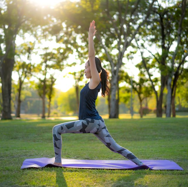 young asian woman practicing warrior 1 yoga in park at sunset