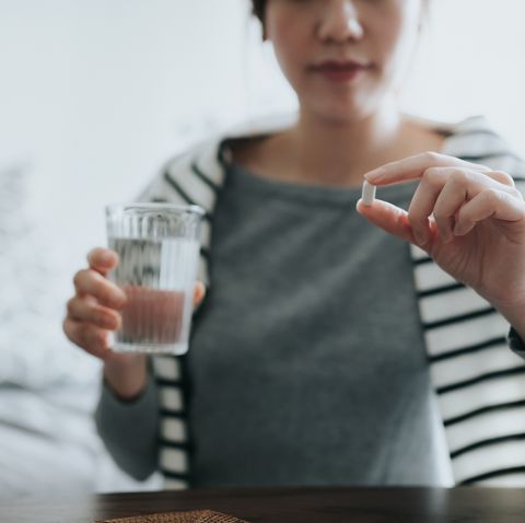 young asian woman taking medicines with a glass of water at homewith a pill bottle by the sidmedicinehealthcare and people concept