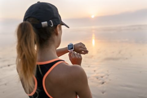 young athlete woman looking the smartwatch on the beach at sunset