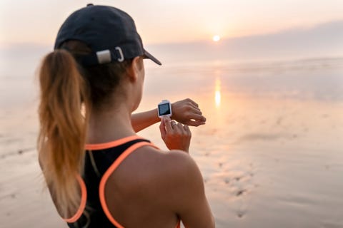 Young athlete woman looking the smartwatch on the beach at sunset