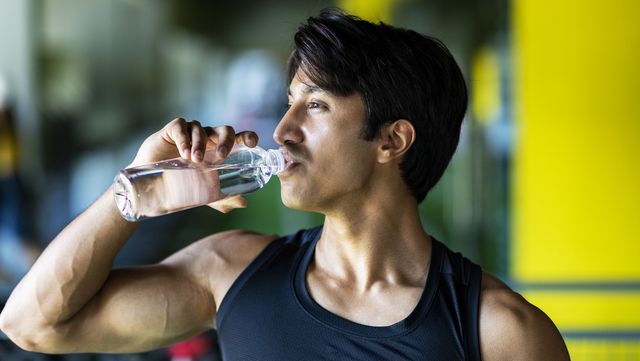 young athletic man drinking water in gym