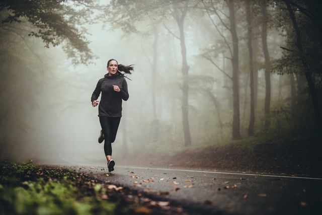 young athletic woman jogging on the road in foggy forest