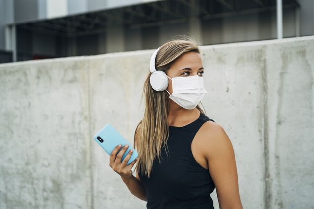 young athletic woman with protective mask, headphones and smartphone