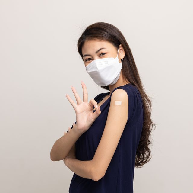 young beautiful asian woman wearing mask and getting a vaccine protection the coronavirus happy female showing arm after receiving vaccination on isolated white background