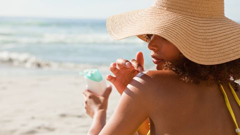 Young beautiful woman applying sunscreen on her shoulder
