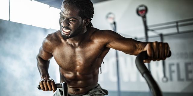 young black athlete making an effort while exercising on stationary bike in a gym