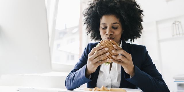 young businesswoman eating hamburger at her desk