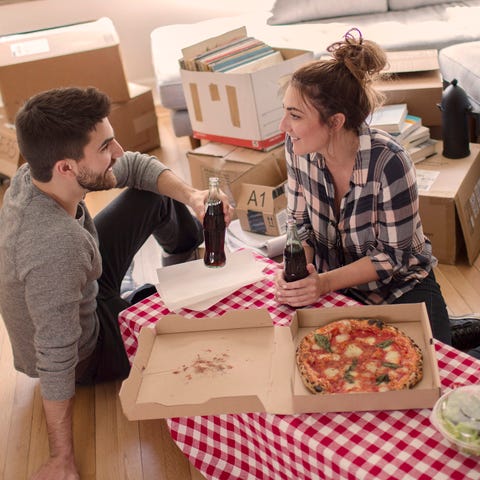 Moving house: Young couple eat pizza in new home, surrounded by boxes
