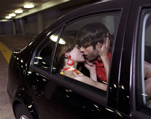 young couple kissing in back of car, view through car window