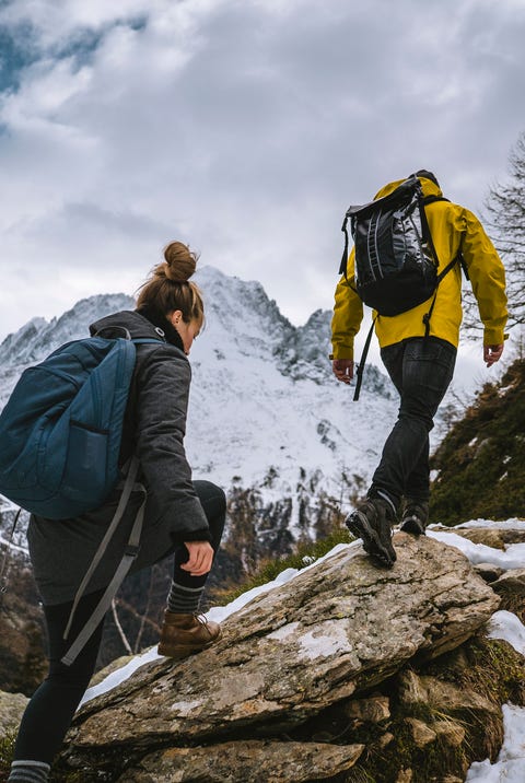 young couple of backpackers hike along a snowy ridge in the mountains