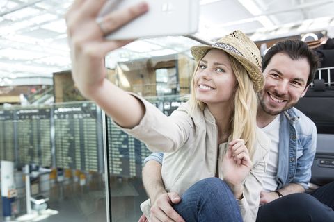 Young couple taking smartphone selfie in airport terminal