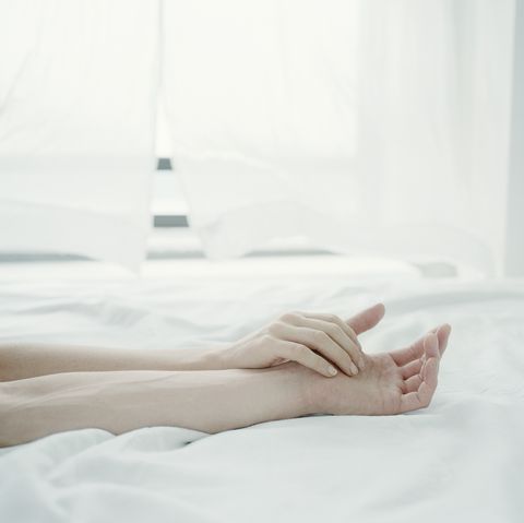 Young couple's arms on bed, hands touching