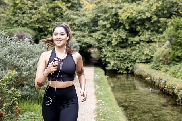 young female runner listening to earphones while running on riverside path