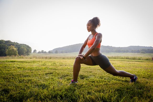 young female runner stretching in rural park