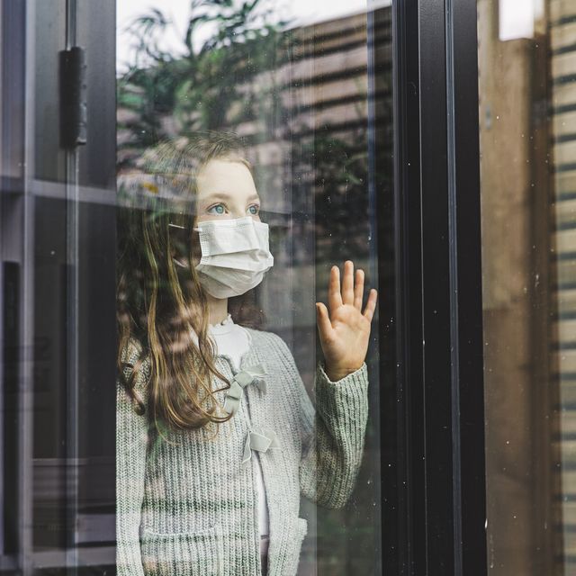 young girl looking through window with mask