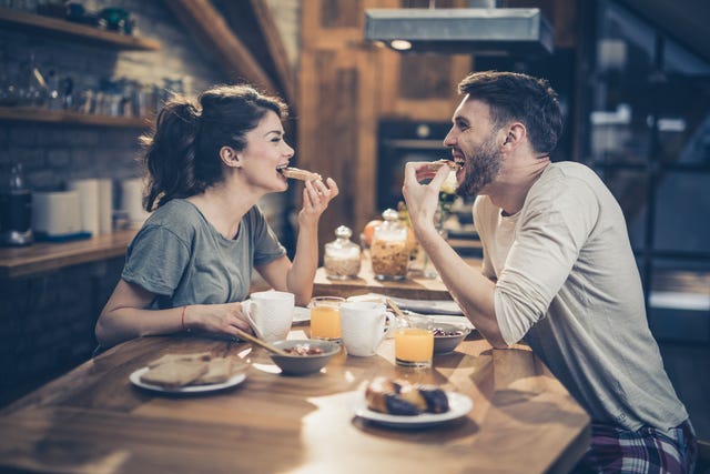 young happy couple having fun while eating sandwiches for breakfast in the kitchen