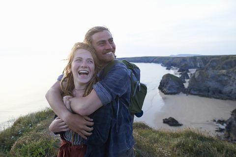 Young hiking couple embracing and laughing on Atlantic coastline.