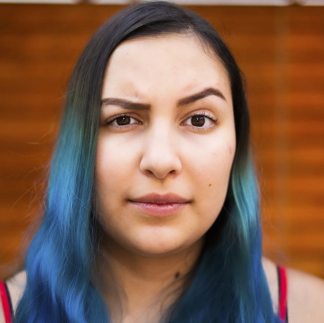 young latino woman with blue hair raising an eyebrow and looking at the camera