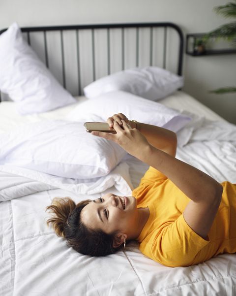 young malaysian woman reading from her phone in bed