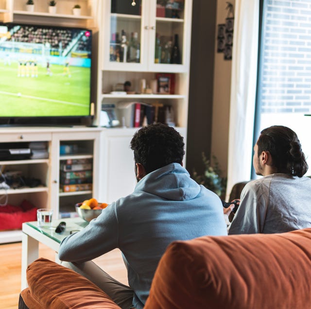 Young male friends playing soccer game on television in living room at home young male friends playing soccer game on television in living room at home
