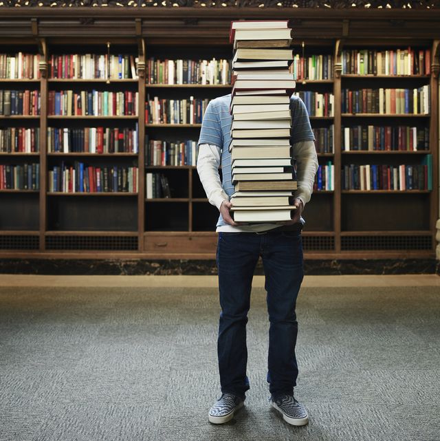 young man carrying stack of books in university library