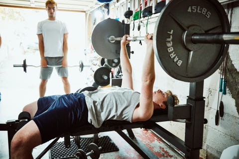 Junger Mann, der Bankdrücken macht, während er mit Freunden im Fitnessstudio in der Garage trainiert