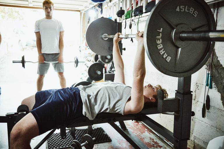 ung man gör bänkpressar medan du tränar med vänner i gymmet i garaget