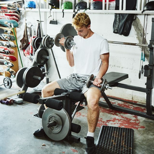 Young man doing bicep curls while working out with friends in gym in garage