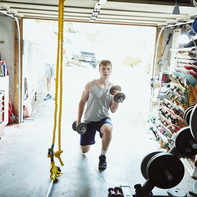 young man doing lunges with dumbbells in gym in garage