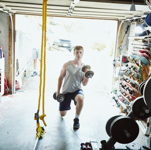 young man doing lunges with dumbbells in gym in garage