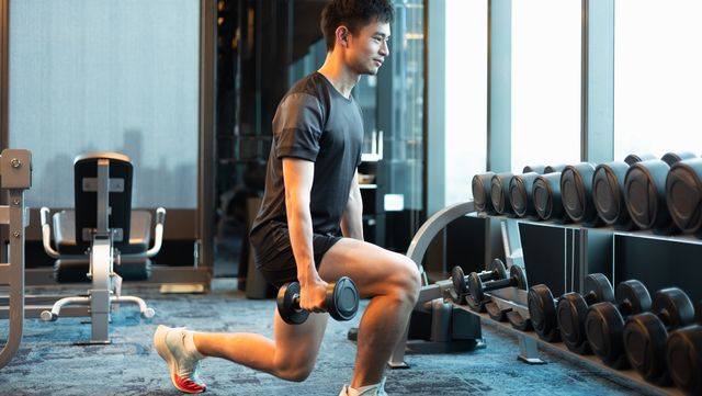 young man doing lunges with dumbbells in gym