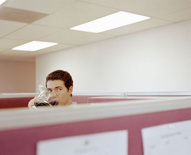 young man drinking coffee from pot in office cubicle