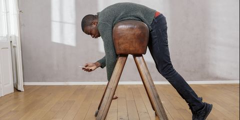 Young man hanging out on pommel horse looking at smartphone