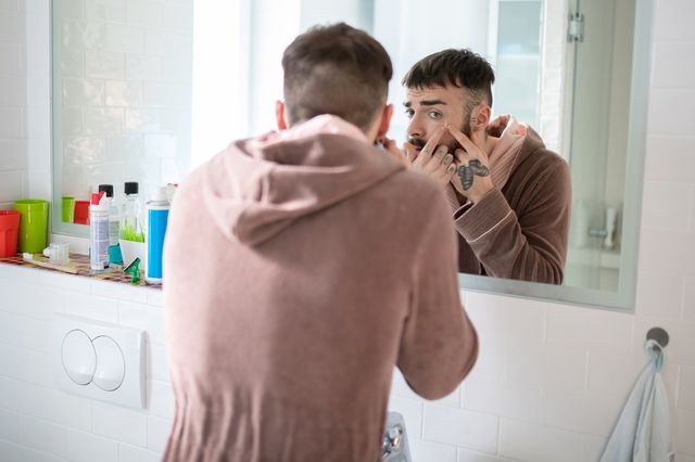 young man in bathrobe in front of the bathroom mirror squeezing blackheads
