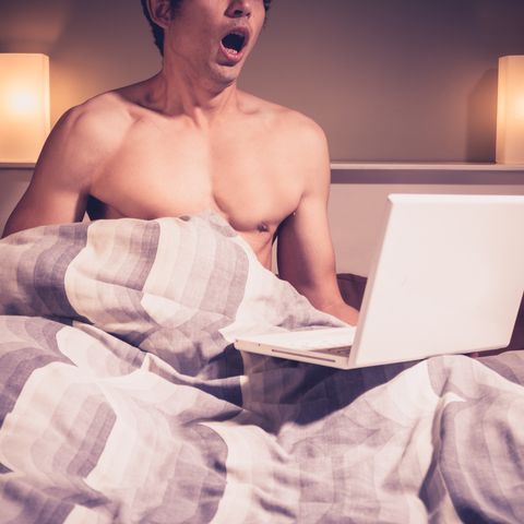 young man in bed watching pornography on laptop