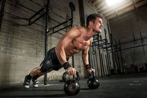 Young man performing press ups on kettlebells in gym