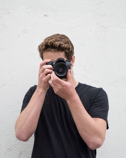 Young Man Photographing With Camera Against Wall