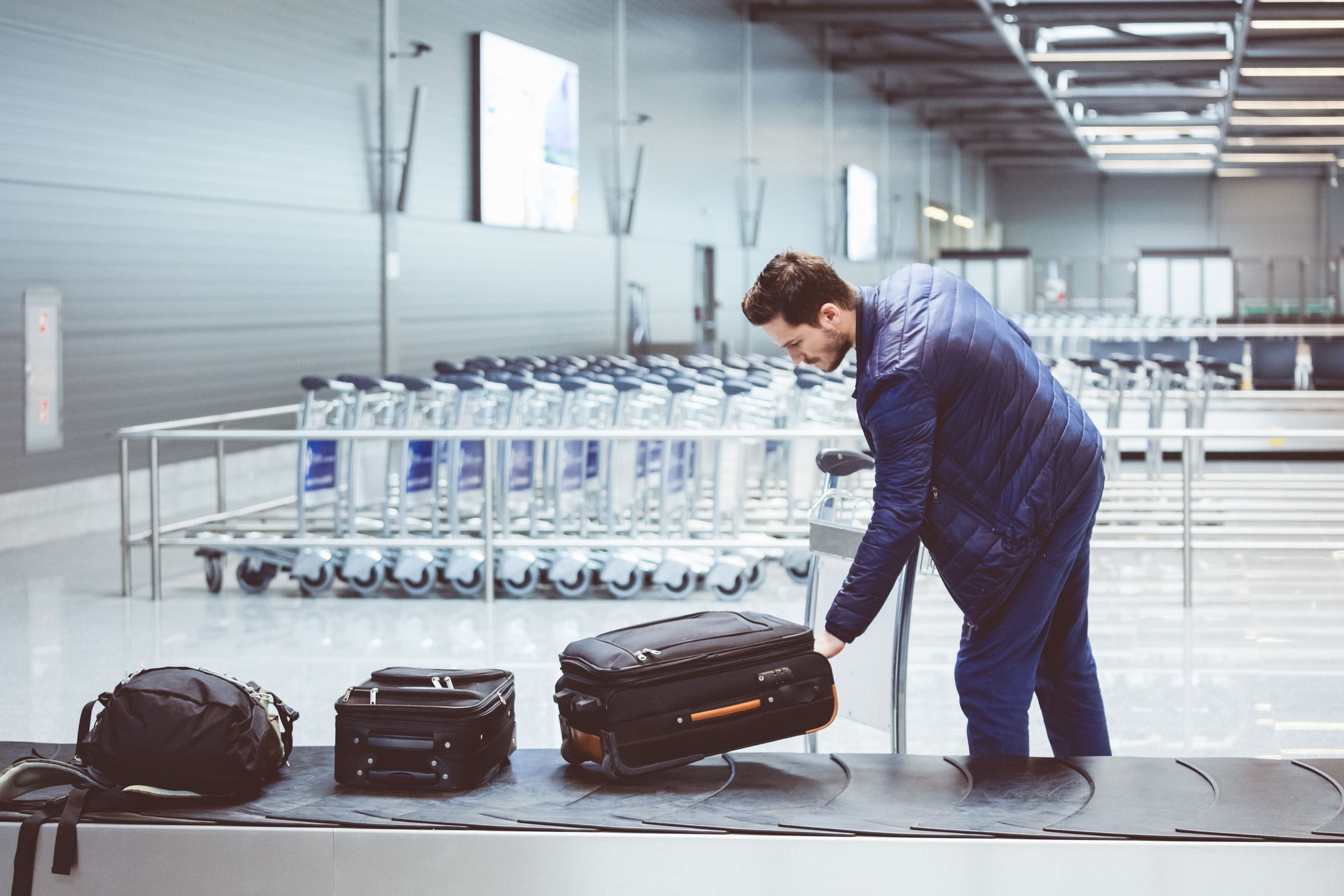 https://hips.hearstapps.com/hmg-prod.s3.amazonaws.com/images/young-man-picking-luggage-from-conveyor-belt-in-royalty-free-image-1657574372.jpg