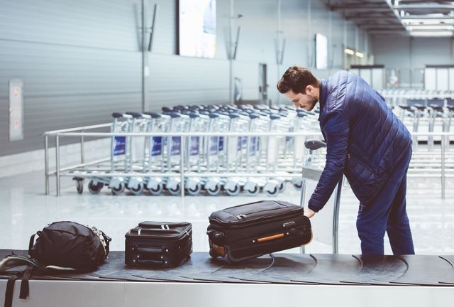 young man picking luggage from conveyor belt in airport