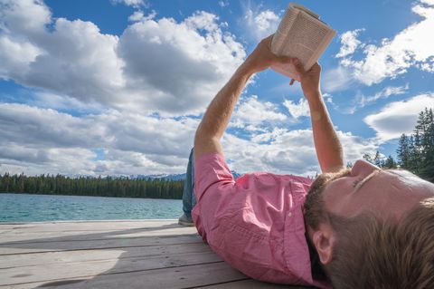 Young man relaxing on lake pier with book