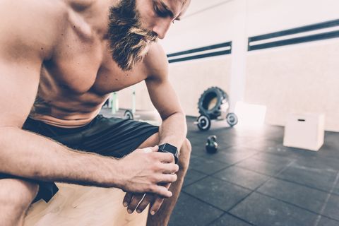 young man sitting checking smartwatch in cross training gym