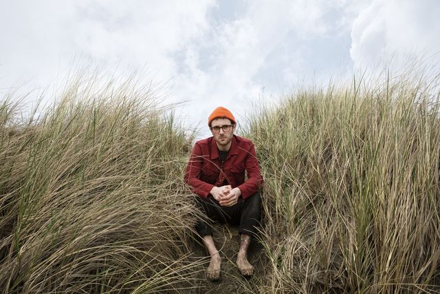 a young man sitting in the dunes with his hands crossed looking into camera